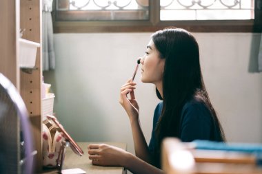 Bekârlık sağlık yaşam tarzını gündüz konseptine hazırlar. Genç Asyalı kadın makyajı ve yüz derisi aynanın önünde evdeki elbise odasında.. 