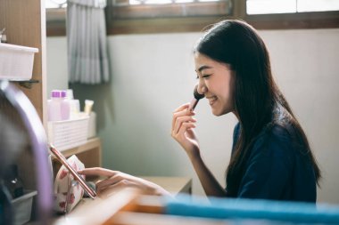 Bekar olmak, sağlıklı ve mutlu bir yaşam tarzını gündüz konseptine hazırlar. Genç Asyalı kadın makyajı ve yüz derisi aynanın karşısında evdeki elbise odasında. Sosyal mesaj uygulaması için cep telefonu kullanılıyor.