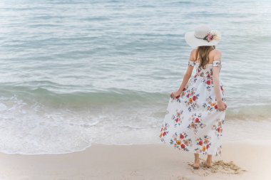 Elbisesi ve şapkası olan Asyalı genç bir kadın sahilde dinleniyor. Pattaya, Tayland