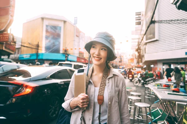 幸せな若い大人のアジアの女性旅行者を歩く青の帽子とバックパックを着用 都会の屋外でデジタルタブレット現代的なライフスタイルでソロ旅行 中華街のストリートフード市場 バンコク — ストック写真