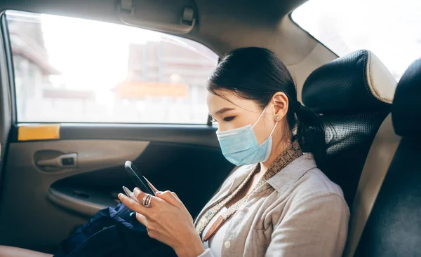 Arabada halk sağlığı için yüz maskesi takan genç Asyalı kadın. Taksi şoförü ve harita için cep telefonu uygulaması kullanılıyor. Bekar insanlar şehir seyahati yaşam tarzı konseptinde taşınır..