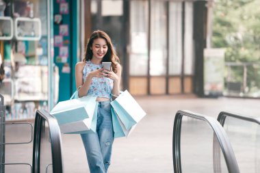 Güzel bir gülümseme genç Asyalı kadın akıllı telefon alışverişi yapıyor ve internetten ödüyor. Bayram indirimi konsepti alışverişi. Şehir kızı yaşam tarzı mutlu açık hava aktiviteleri.