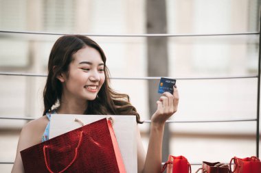 Tatillerde bekâr olmak. Kredi kartı ve alışveriş torbaları tutan genç Asyalı kadın. Nakitsiz konsept ile satın alma.