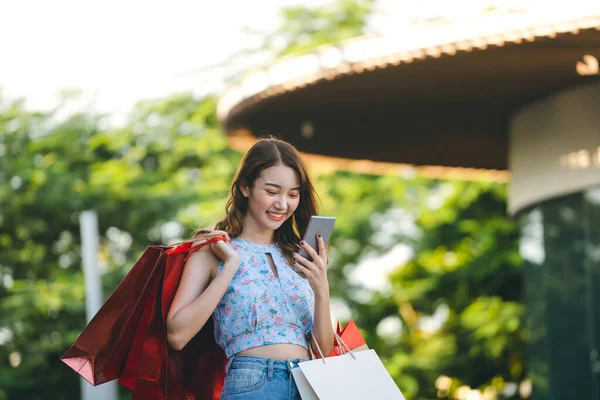 屋外公園での若い大人のアジアの影響力のある女性のショッピング オンラインでの支払いにスマートフォン交換通貨を使用します 夏の販売割引プロモーションコンセプト コピースペースの背景 — ストック写真