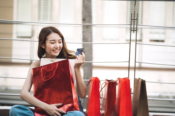 Güzel, genç Asyalı bir kadın kredi kartını elinde tutuyor ve nakit ödemiyor. Bayram indirimi konsepti alışverişi. Şehir kızı yaşam tarzı mutlu açık hava aktiviteleri.