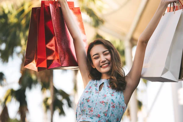 Tatillerde bekâr olmak. Alışveriş torbalarıyla büyüyen mutlu, genç Asyalı kadın. Kopyalama alanı olan arkaplan.