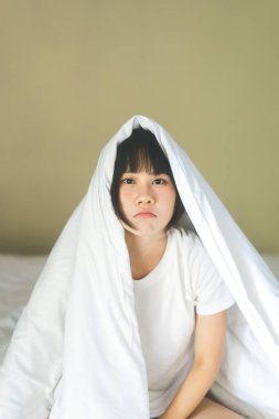 Asyalı genç bir kadının portresi. Kadın insanlar uyandıktan sonra yatak odasında dinlenir. Göz kamaştırıcı bir kamerayla evde kalırlar. Battaniyeli beyaz gömlek giy..