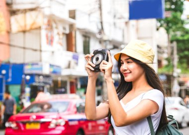Sırt çantalı, beyaz gömlekli genç Asyalı gezgin kadın. Elinde fotoğraf makinesi var. Khaosan caddesinin yanında. Bangkok Şehri, Tayland