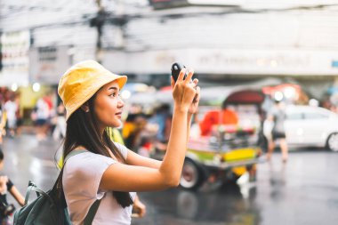 Sırt çantalı, beyaz gömlekli, mutlu Asyalı genç bir kadın. Yaowarat 'ın yanında fotoğraf makinesi ile fotoğraf çekmek. Çin Mahallesi sokak yemekleri. Bangkok Şehri, Tayland