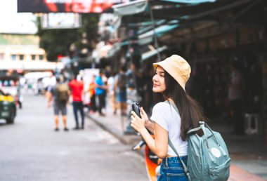 Sırt çantalı, beyaz gömlekli, mutlu Asyalı genç bir kadın. Kamerayı tutuyorum. Khaosan Yolu 'ndaki tarihi cadde pazarının yanında. Bangkok Şehri, Tayland
