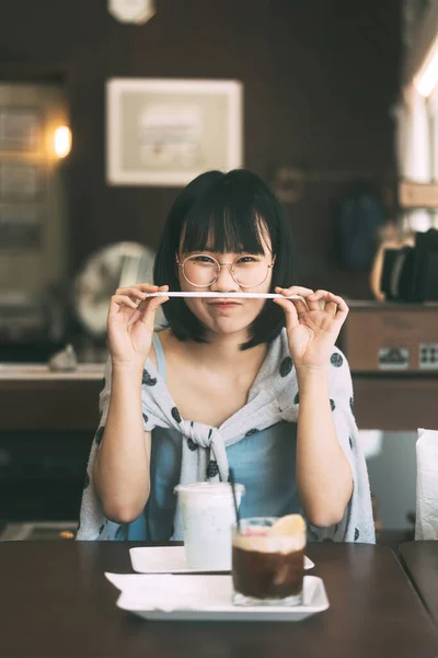 幸せな若い大人のアジアの女性のカメラの肖像画を見ます眼鏡をかけますコーヒーカフェ屋内で日 — ストック写真