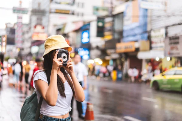 Sırt çantalı, beyaz gömlekli, mutlu Asyalı genç bir kadın. Yaowarat 'ın yanında fotoğraf makinesi ile fotoğraf çekmek. Çin Mahallesi sokak yemekleri. Bangkok Şehri, Tayland