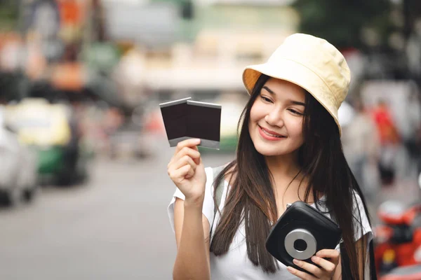 若い大人のアジアの旅行者の幸せな女性の白いシャツのバックパックのソロ旅行のコンセプト インスタントカメラフィルムの写真を保持 カオサン通りで 観光地ランドマーク バンコク — ストック写真