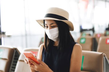 Havaalanı terminali sosyal uzaklık başkanı Corona virüsü salgını oluşturuyor. Genç, yetişkin bir turist kadın maske takıyor ve kovid 19 'dan koruyor. Başlangıç yolculuğu için cep telefonuyla giriş yapın.