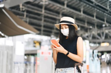 Havaalanı terminali sosyal mesafelendirme Corona virüsü salgını. Genç, yetişkin bir turist kadın maske takıyor ve kovid 19 'dan koruyor. Cep telefonuyla kontrol et. İnsanlar yeni normal yaşam tarzı konseptiyle seyahat ederler.