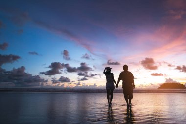Yaz tatilinde, Asyalı turist bir çiftin el ele tutuşması. Doğada plaj denizinde güzel alacakaranlık günbatımı gökyüzü ile rahatlayın. Yurt içi seyahat, Phuket, Tayland.