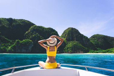 Yetişkin bir kadının arka görüntüsü yelkenli teknede oturur ve rahatlar sarı bikinili mavi gökyüzü ve deniz. Maya Körfezi 'nde yaz tatili ada gezisi. Yengeç, Tayland