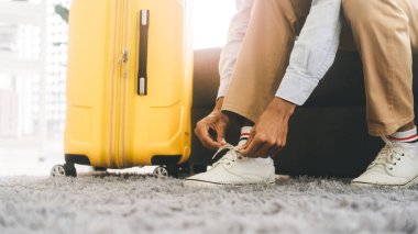 Asyalı turist, bağcıklarını bağlamak için bavulla yolculuğa çıktı. İnsanlar tatil gezisine hazırlanıyor. Kopyalama alanı olan arkaplan.