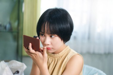 Bekar portresi sağlıklı yaşam tarzını gündüz konseptine hazırlar. Genç Asyalı kadın makyajı ve yüz bakımı aynanın karşısında evdeki elbise odasında..