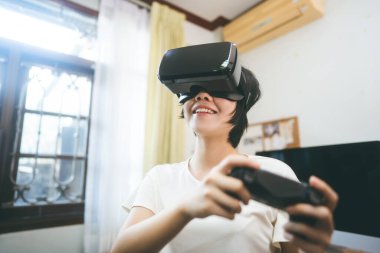 VR teknolojisi olan genç Asyalı kadın yaşam tarzı. Çevrimiçi siber medya için sanal gerçeklik kulaklığı takıyor. Evde rahatla hobi olarak geleceğin modasına uygun bir internet oyunu oyna..