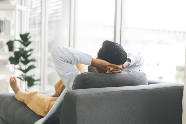 Rear view of adult man relax on sofa couch at home. People rest time in living house for nap or calm. Blur background with window light and copy sapce.