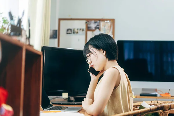 Young adult asian woman stay and work from home office concept. Business female using smart phone via internet online. Background with computer indoor on day.