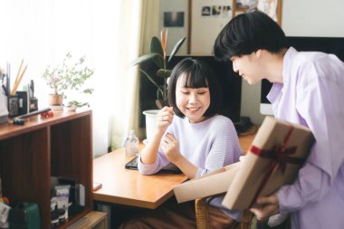 Genç, güneydoğu Asyalı aşk çifti birlikte yaşıyor. Mutlu yüzlü kadın sevgilisinden sürpriz yıldönümü hediyesi almış. Kutlama için romantik anlar.