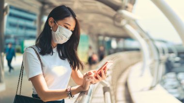 Young adult business asian working woman wear face mask for protect virus corona or covid19 and air pollution. Using mobile phone application. Urban people lifestyle with public health on day concept.