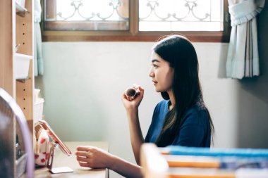 Bekar olmak, sağlıklı ve mutlu bir yaşam tarzını gündüz konseptine hazırlar. Genç Asyalı kadın makyajı ve yüz derisi aynanın karşısında evdeki elbise odasında. Sosyal mesaj uygulaması için cep telefonu kullanılıyor.