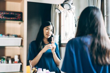 Bekar portresi sağlıklı yaşam tarzını gündüz konseptine hazırlar. Genç Asyalı kadın makyajı ve yüz derisi aynanın önünde evdeki elbise odasında.. 