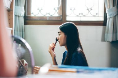 Bekar olmak, sağlıklı ve mutlu bir yaşam tarzını gündüz konseptine hazırlar. Genç Asyalı kadın makyajı ve yüz derisi aynanın önünde evdeki elbise odasında..