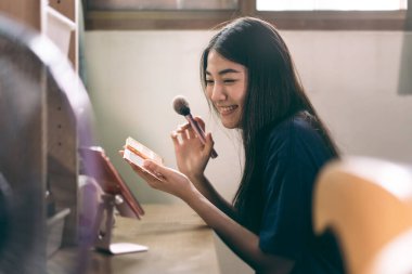 Bekar olmak, sağlıklı ve mutlu bir yaşam tarzını gündüz konseptine hazırlar. Genç Asyalı kadın makyajı ve yüz derisi aynanın karşısında giyinme odasında ve mobil uygulama ile canlı yayında..