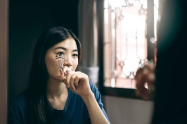 Bekârlık sağlık yaşam tarzını gündüz konseptine hazırlar. Genç Asyalı kadın makyaj kirpiği ve yüz derisi aynanın karşısında evdeki soyunma odasında.. 