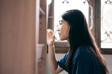 Bekârlık sağlık yaşam tarzını gündüz konseptine hazırlar. Genç Asyalı kadın makyaj kirpiği ve yüz derisi aynanın karşısında evdeki soyunma odasında.. 
