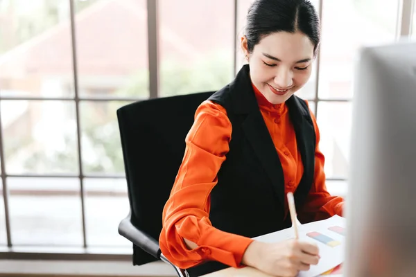 快乐微笑的形象写字楼生意亚洲的薪水女人 有文档和计算机的工作场所 她在桌上写了一个启动项目 有窗灯的背景 — 图库照片