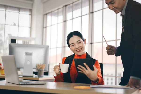 亚洲成年人的笑业务与技术 女商人手握平板电脑检查股票的销售情况 在工作场所喝咖啡放松点 最小办公室窗口灯光背景 — 图库照片