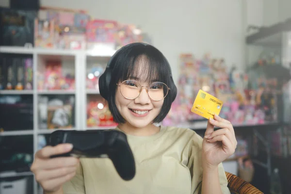オタクスタイルの若い大人のアジアのゲーマーの女性は眼鏡を着用し ヘッドフォンゲームをプレイします 支払いにクレジットカードを使用して勝つとショッピング — ストック写真