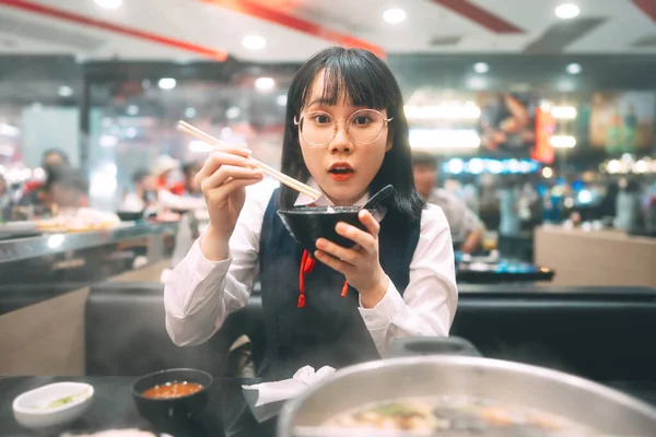 People city break enjoy eating food lifestyle concept. Happy young asian woman in japanese uniform student at shabu japan sukiyaki restaurant. Hot pot with smoke. Enjoy foodie tasty time.