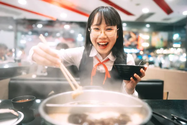 People city break enjoy eating food lifestyle concept. Happy young asian woman in japanese uniform student at shabu japan sukiyaki restaurant. Hot pot with smoke. Enjoy foodie tasty time.