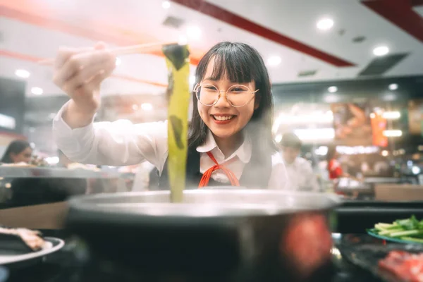 People city break enjoy eating food lifestyle concept. Happy young asian woman in japanese uniform student at shabu shabu japan sukiyaki restaurant. Hot pot with smoke. Enjoy foodie tasty time.