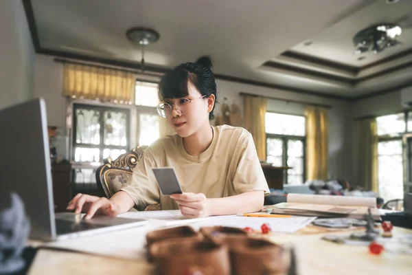 Role playing tabletop and board games hobby concept. Young adult asian woman using laptop for streaming online with friends. On table with blur dice and miniatures.