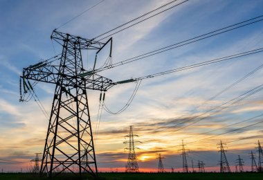 Yüksek voltajlı elektrik hatlarının silueti gün doğumunda ya da günbatımında renkli bir gökyüzüne karşı.