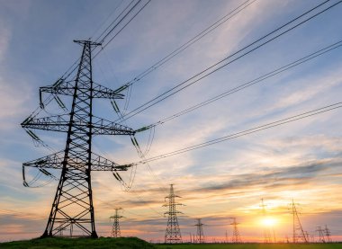 Yüksek voltajlı elektrik hatlarının silueti gün doğumunda ya da günbatımında renkli bir gökyüzüne karşı.