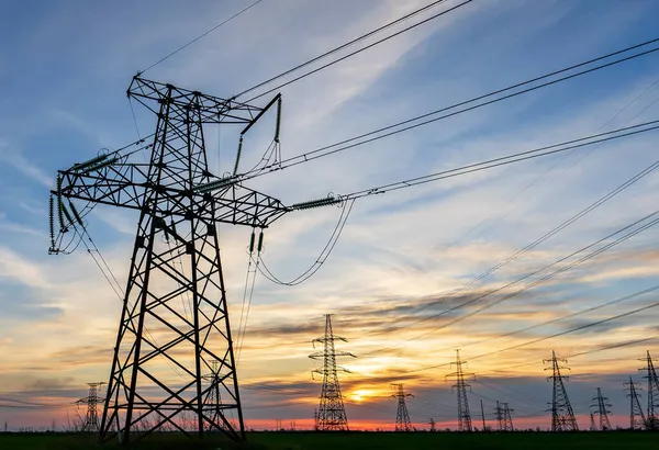 Yüksek voltajlı elektrik hatlarının silueti gün doğumunda ya da günbatımında renkli bir gökyüzüne karşı.