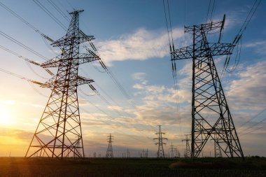 Yüksek voltajlı elektrik hatlarının silueti gün doğumunda ya da günbatımında renkli bir gökyüzüne karşı.