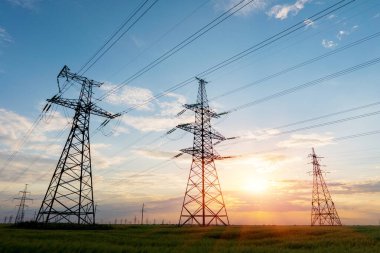 Yüksek voltajlı elektrik hatlarının silueti gün doğumunda ya da günbatımında renkli bir gökyüzüne karşı.
