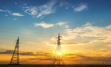 Yüksek voltajlı elektrik hatlarının silueti gün doğumunda ya da günbatımında renkli bir gökyüzüne karşı.