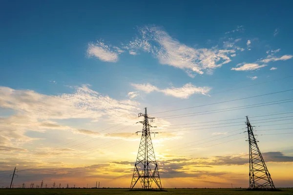 Yüksek voltajlı elektrik hatlarının silueti gün doğumunda ya da günbatımında renkli bir gökyüzüne karşı.