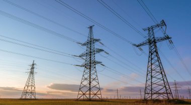 Yüksek voltajlı elektrik hatlarının silueti gün doğumunda ya da günbatımında renkli bir gökyüzüne karşı.