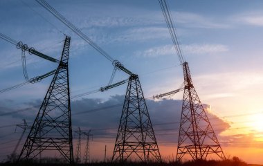 Yüksek voltajlı elektrik hatlarının silueti gün doğumunda ya da günbatımında renkli bir gökyüzüne karşı.